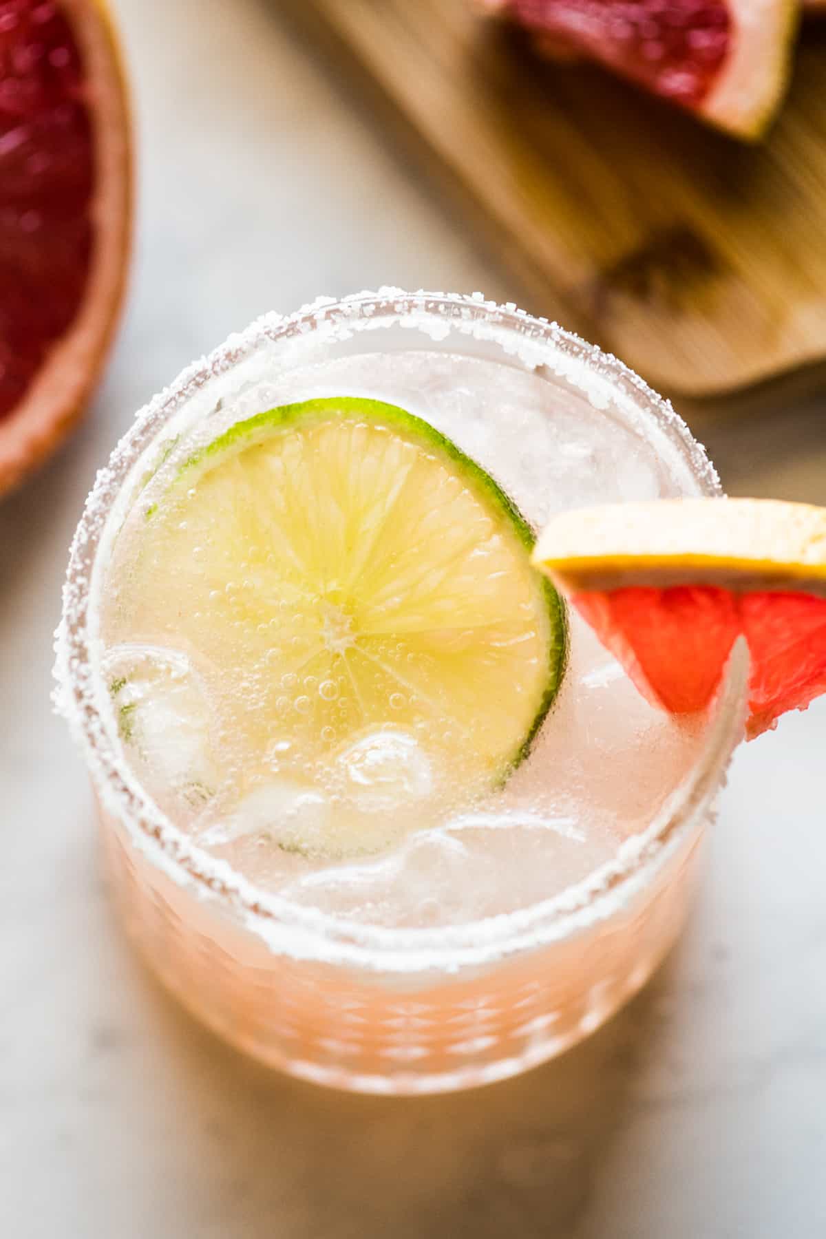 A Paloma drink in an iced glass with a slice of fresh lime and a grapefruit wedge.