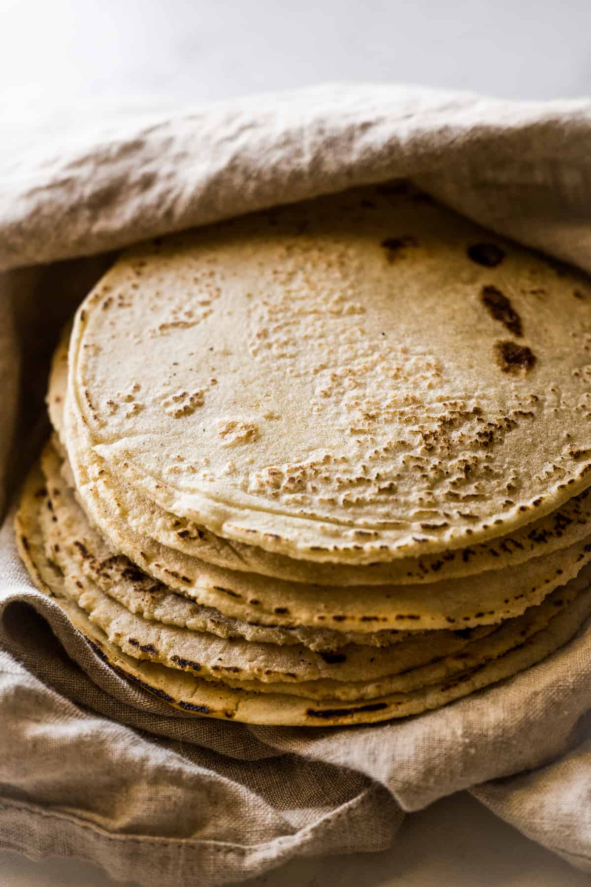 A stack of homemade corn tortillas wrapped in a kitchen towel.