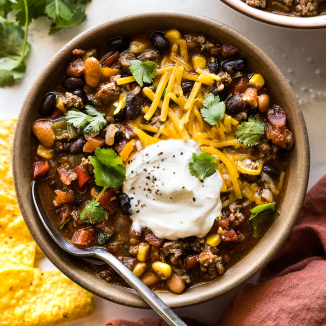 Taco soup in a bowl topped with shredded cheese, sour cream, and cilantro.