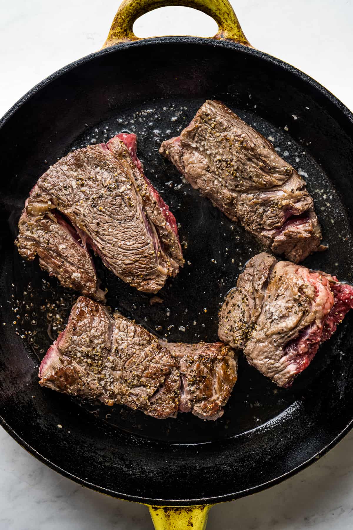 Large skillet with oil and four pieces of beef cooking until browned. 