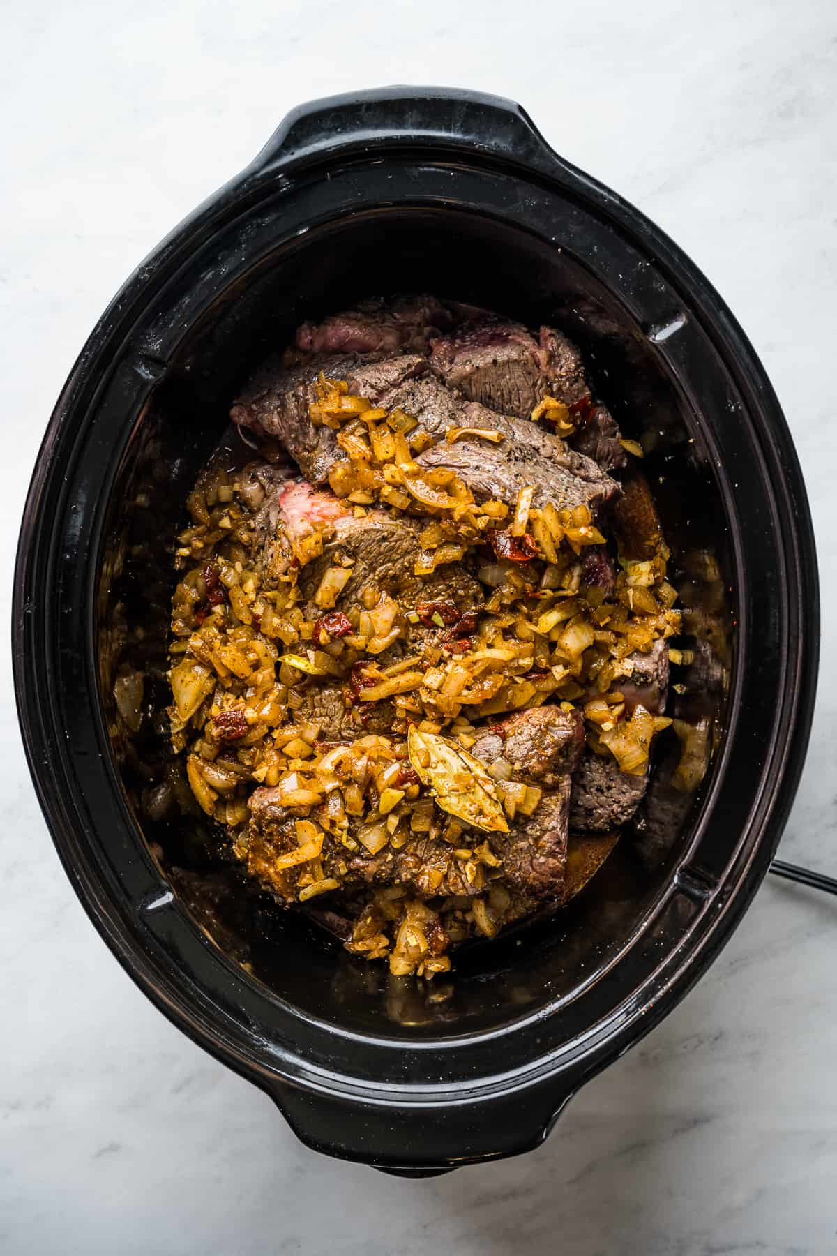 Seared meat and broth mixture in a large slow cooker. 