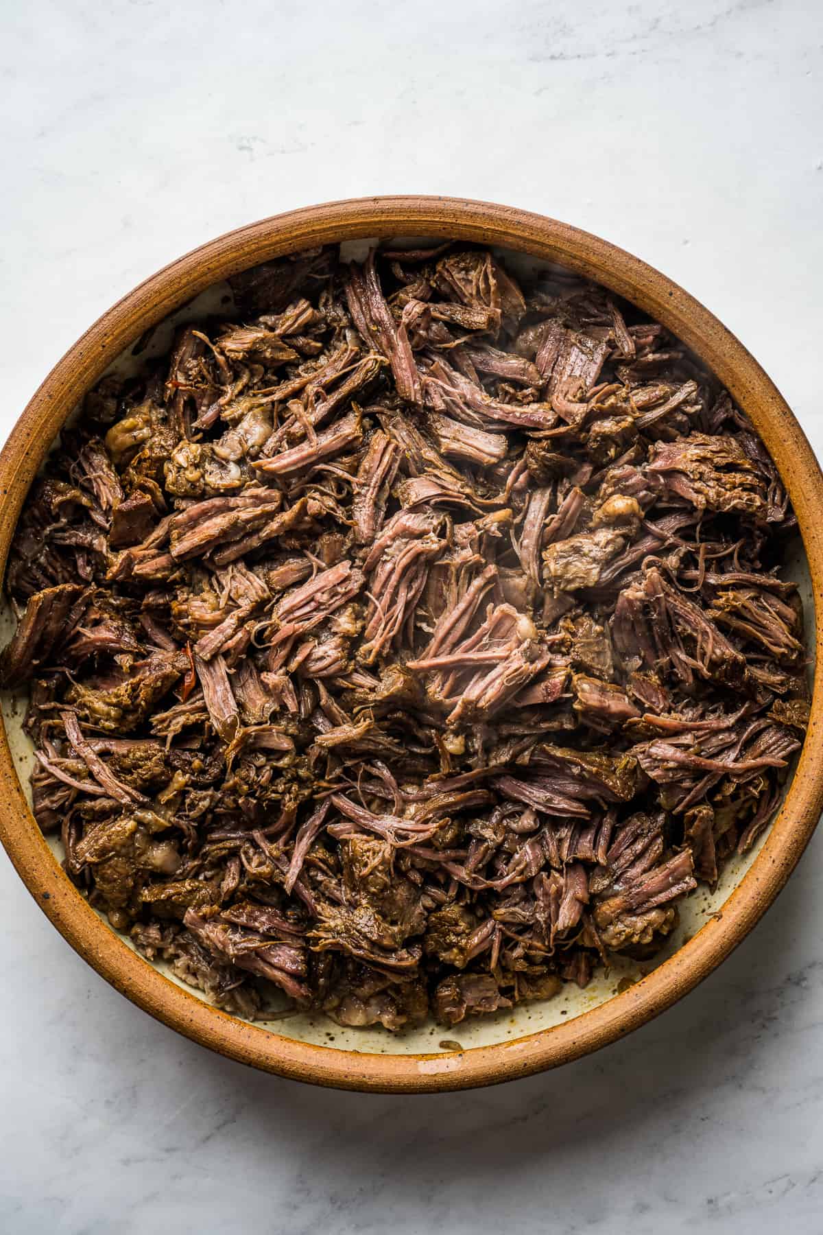 Beef placed in a large bowl to be shredded with two forks. 