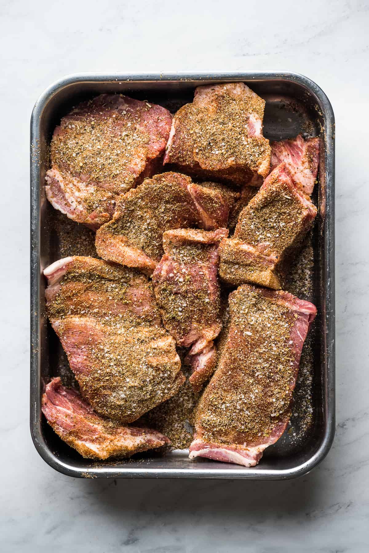Seasoned pork shoulder cut into large chunks on a baking tray.