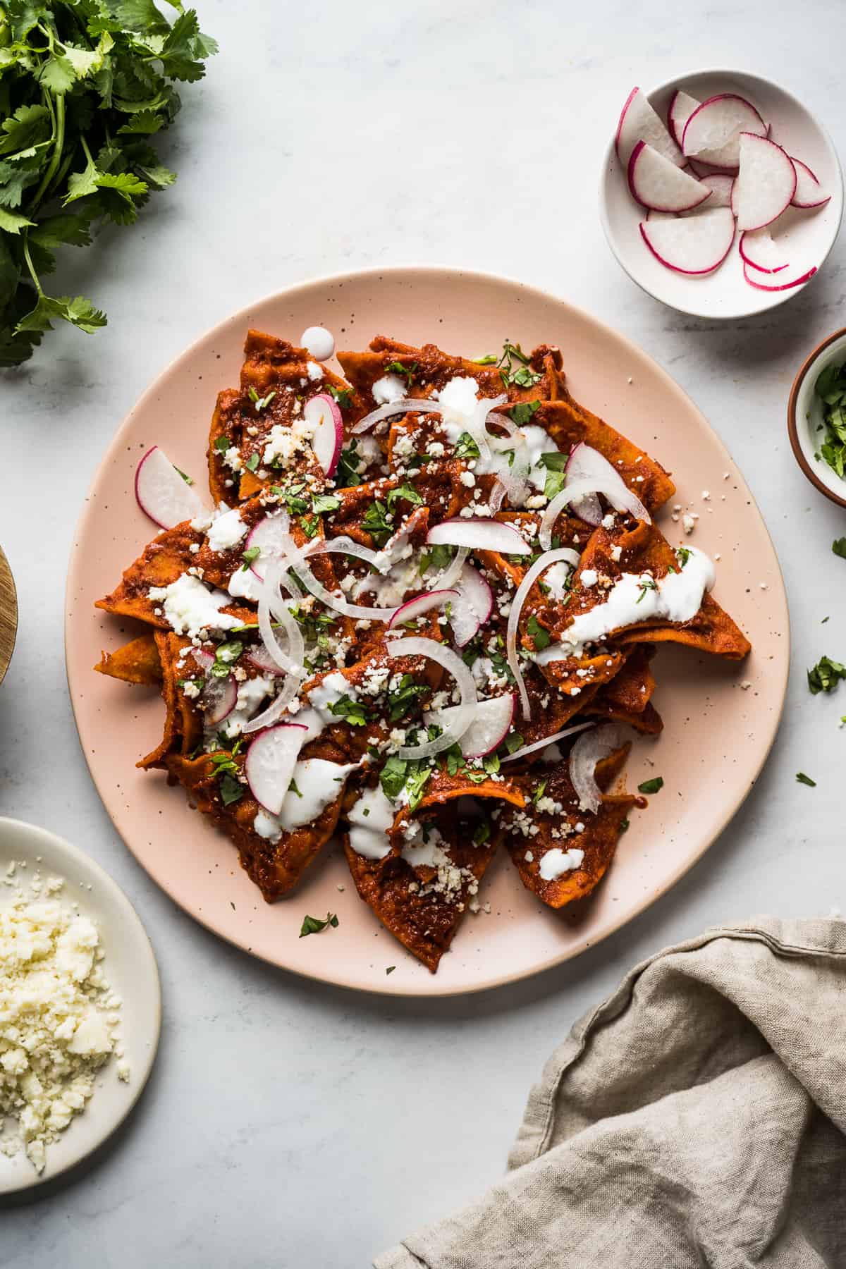 Chilaquiles on a plate with red sauce and topped with Mexican crema, onions, cotija cheese, and cilantro.