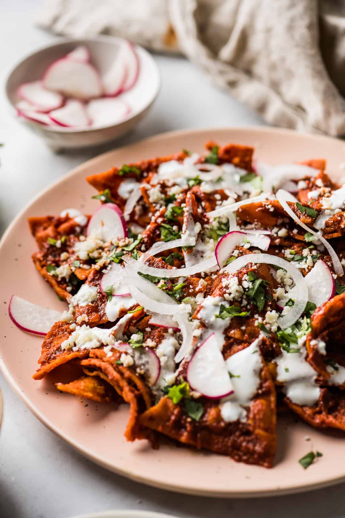 Chilaquiles on a plate topped with cilantro, onions, radishes, and Mexican crema.