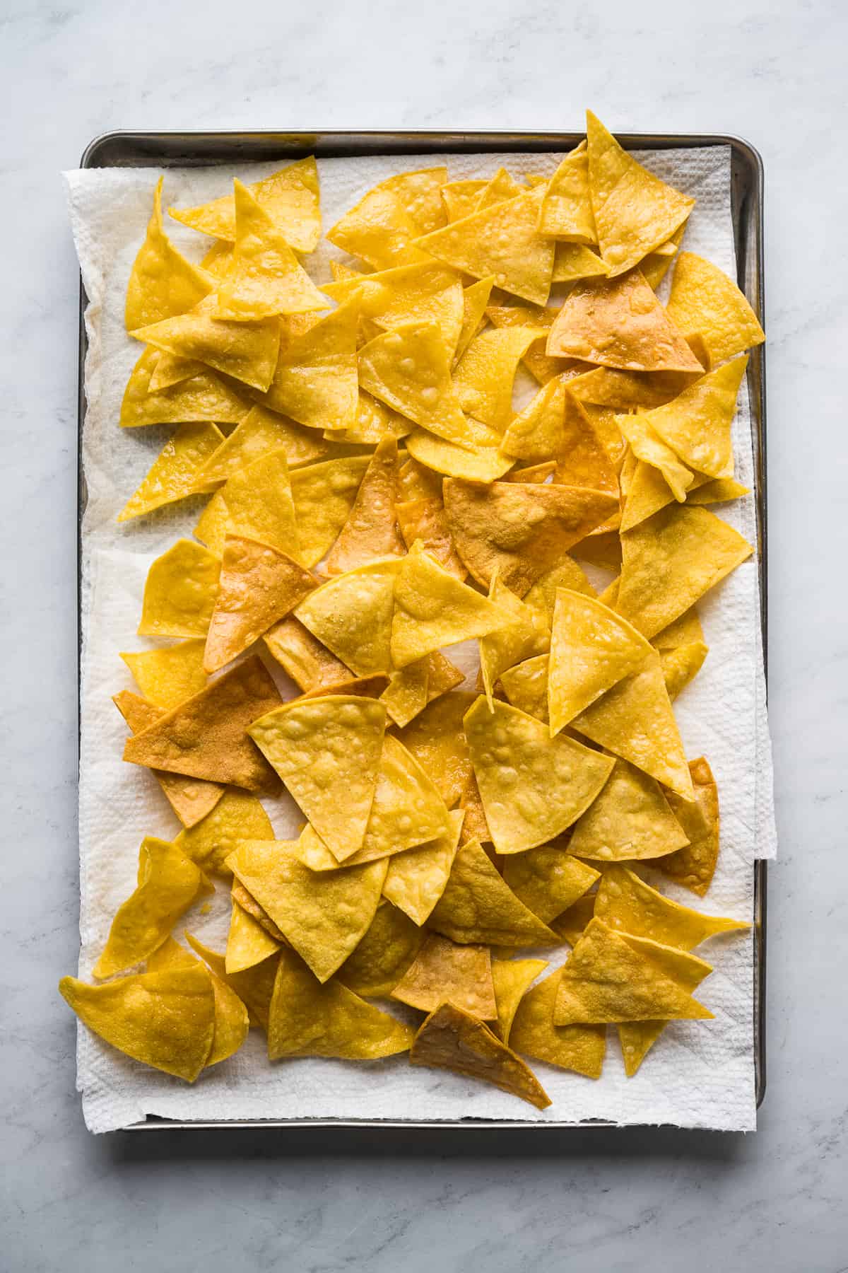 Freshly fried corn tortilla chips on a baking sheet lined with paper towels.