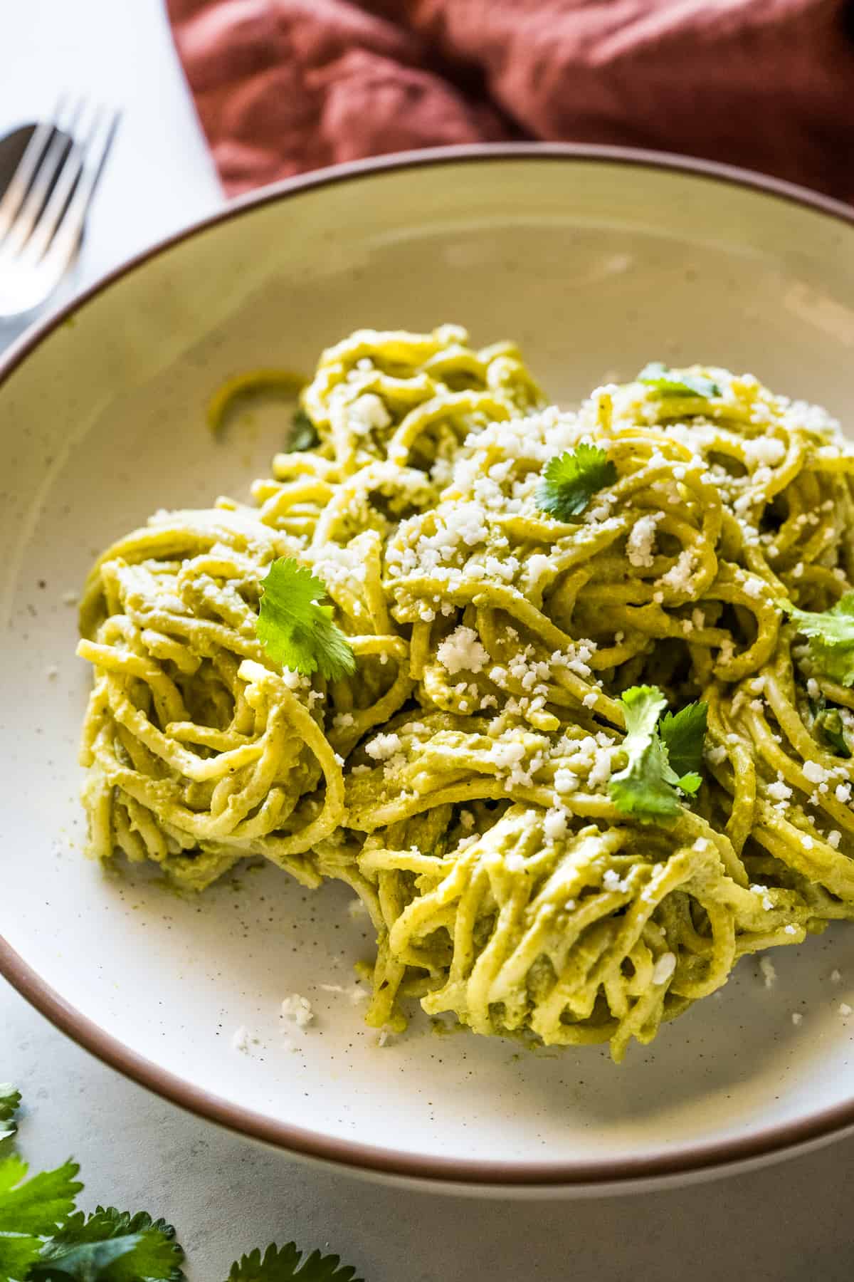 Green Spaghetti (Espagueti Verde) in a bowl topped with Mexican queso fresco and cilantro leaves.