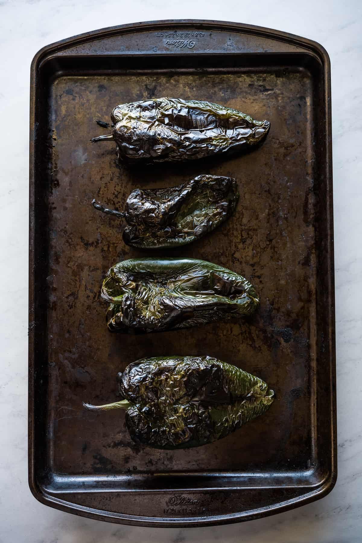 Roasted poblano peppers on a baking sheet.