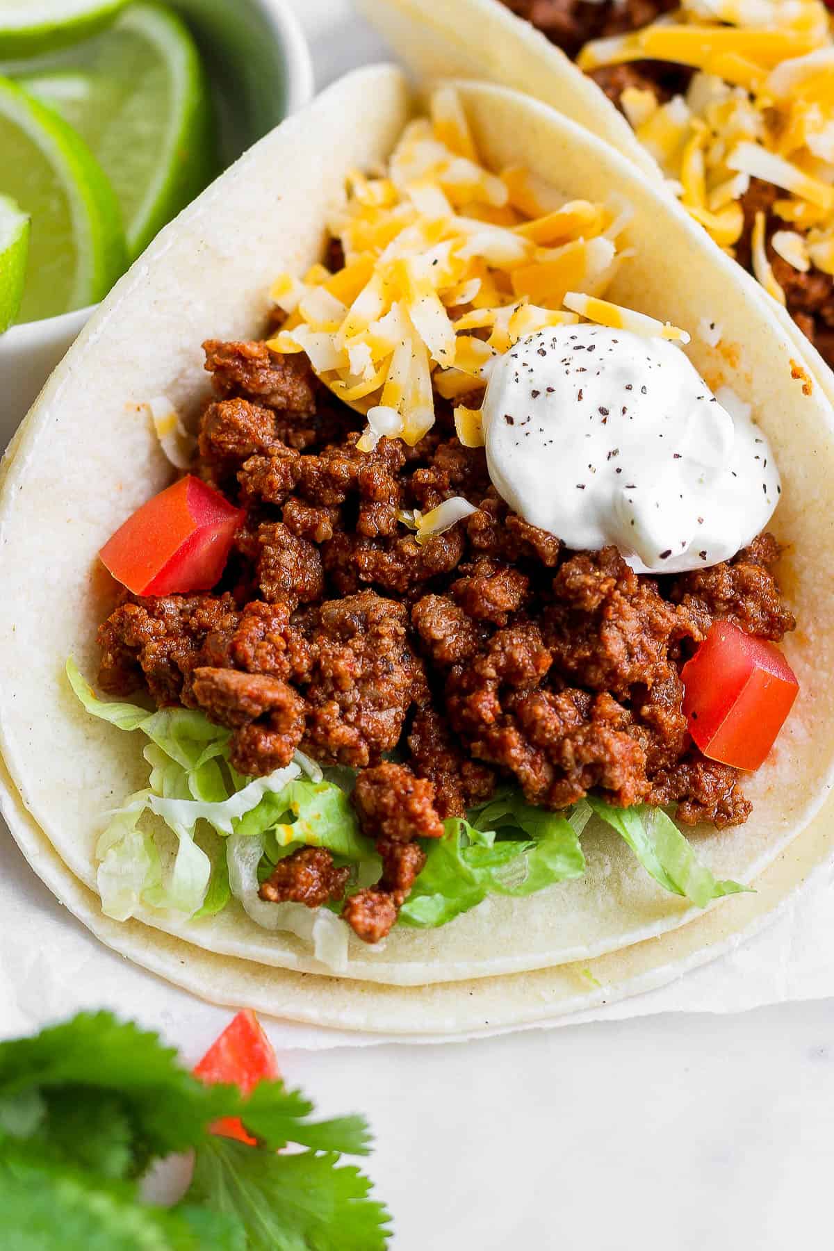 Ground beef tacos in a tortilla topped with shredded lettuce, cheese, sour cream, and diced tomatoes.