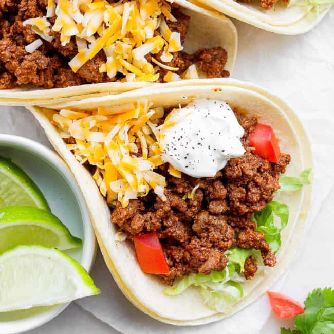 Ground beef tacos topped with shredded cheese, sour cream, and diced tomatoes.