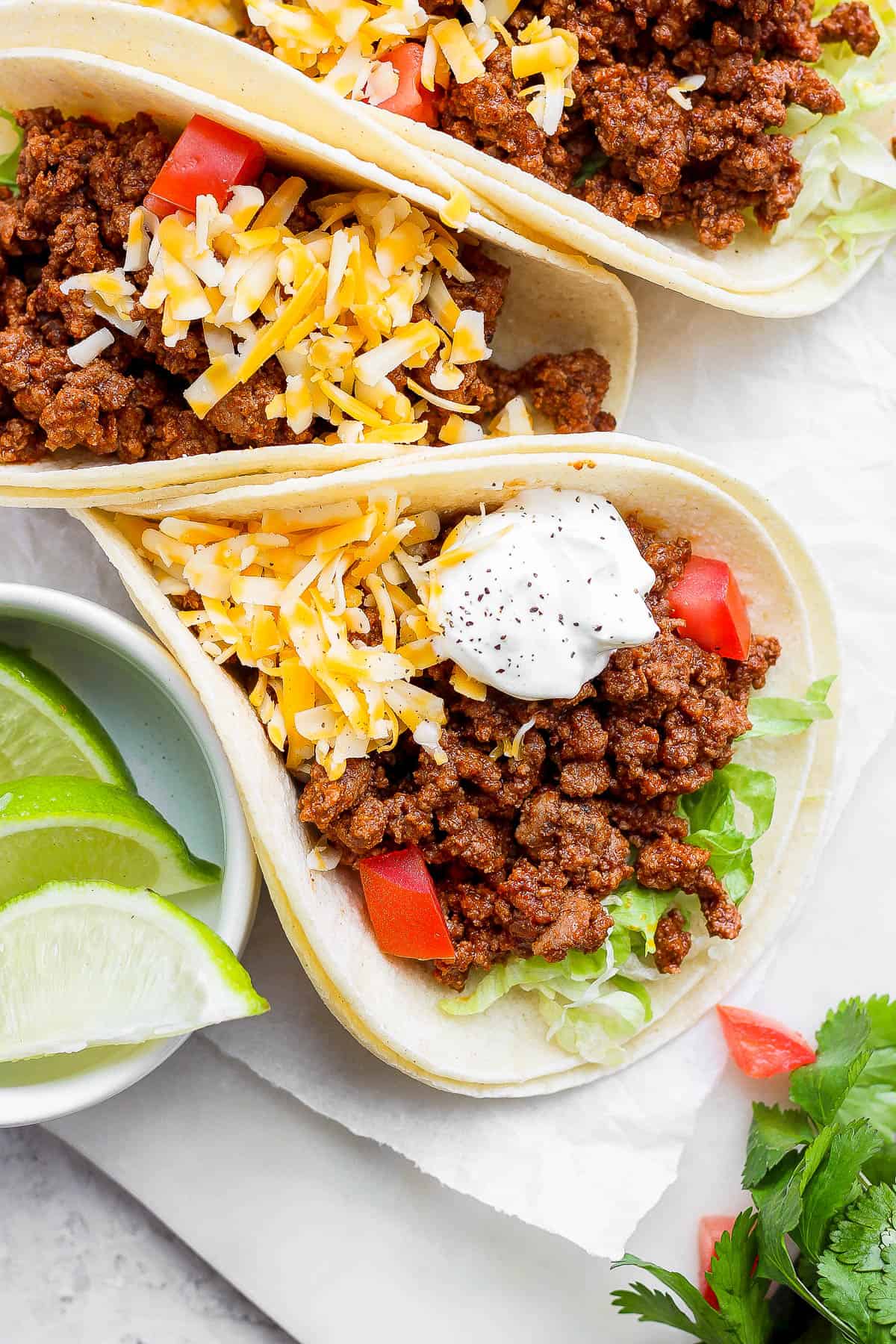 Ground beef tacos topped with shredded cheese, sour cream, and diced tomatoes.