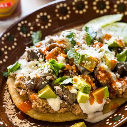 Mexican Huaraches on a plate topped with refried beans, cheese, and more.