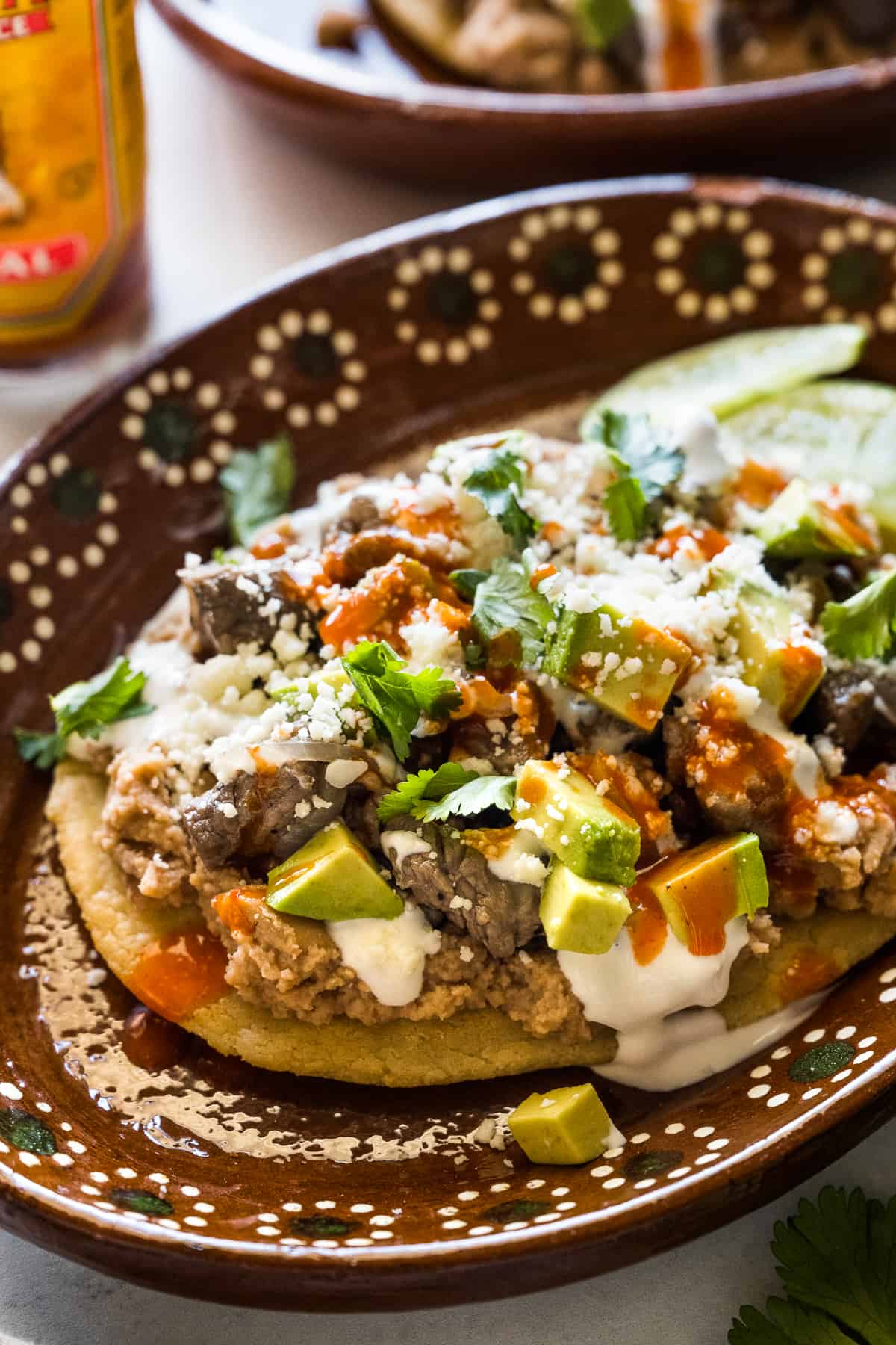 Mexican Huarache on a plate topped with avocado, queso fresco, cilantro, and salsa.