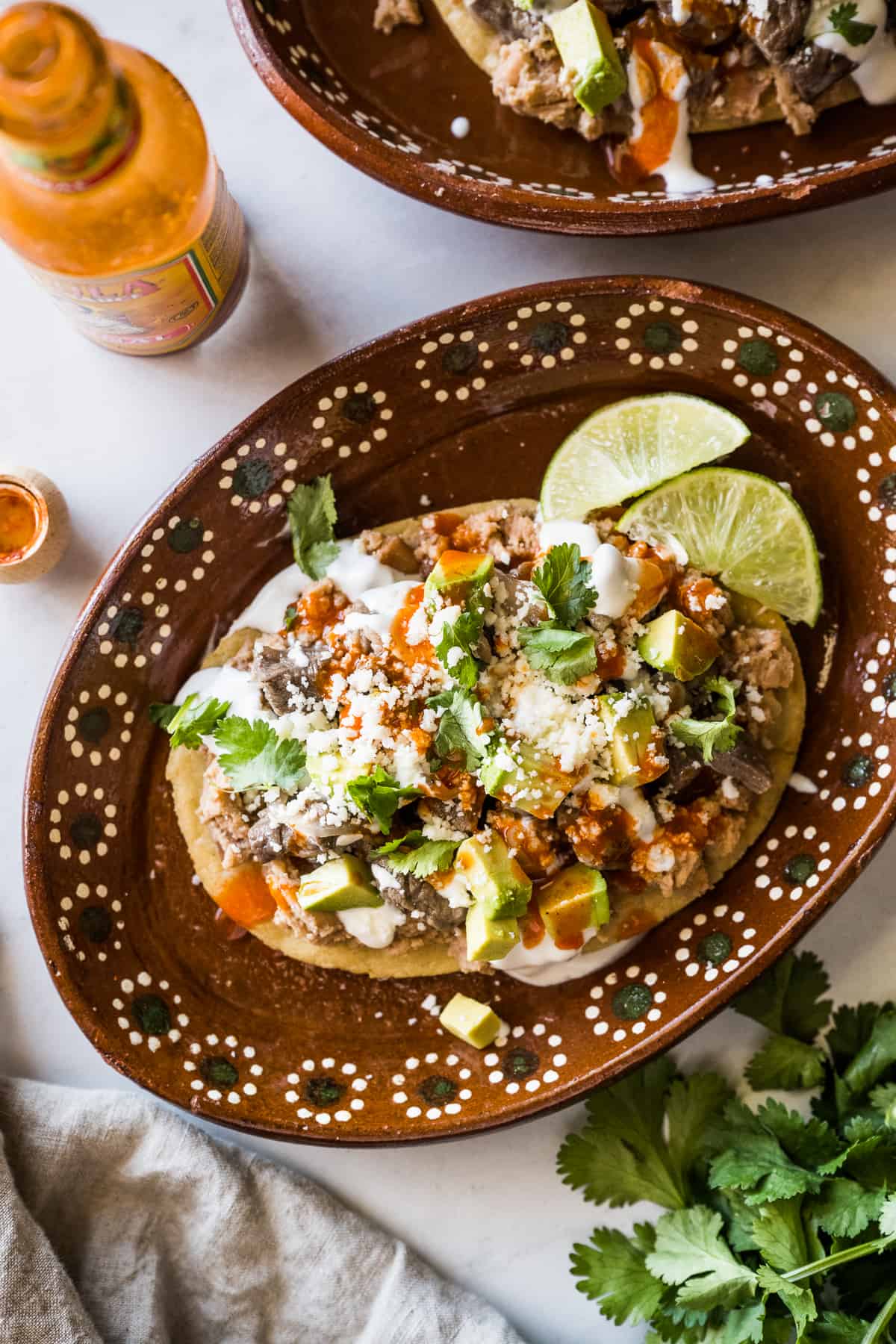 Plated Mexican huarache topped with refried beans, beef, onions, and more.