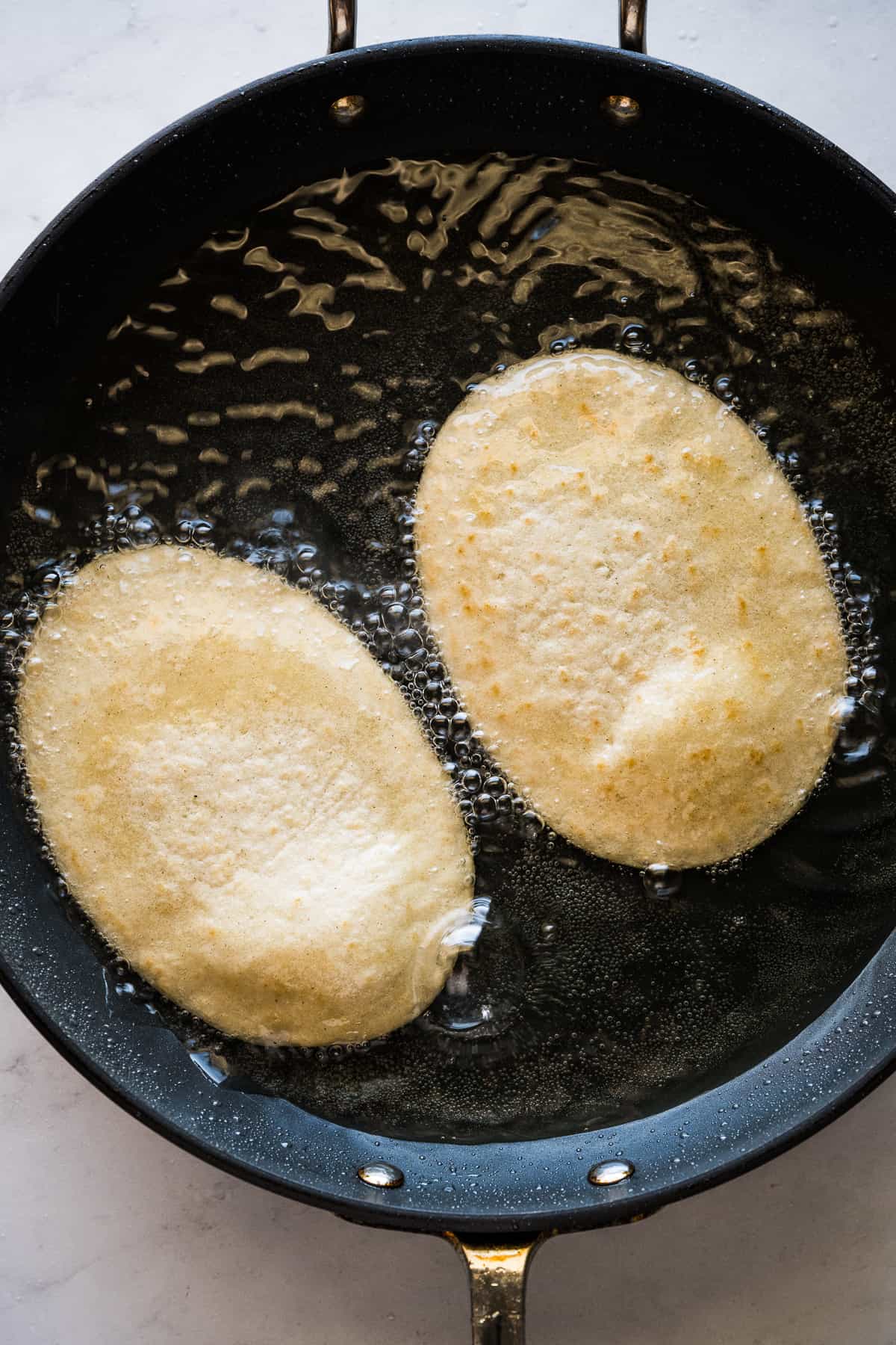 Huaraches being fried in a skillet.