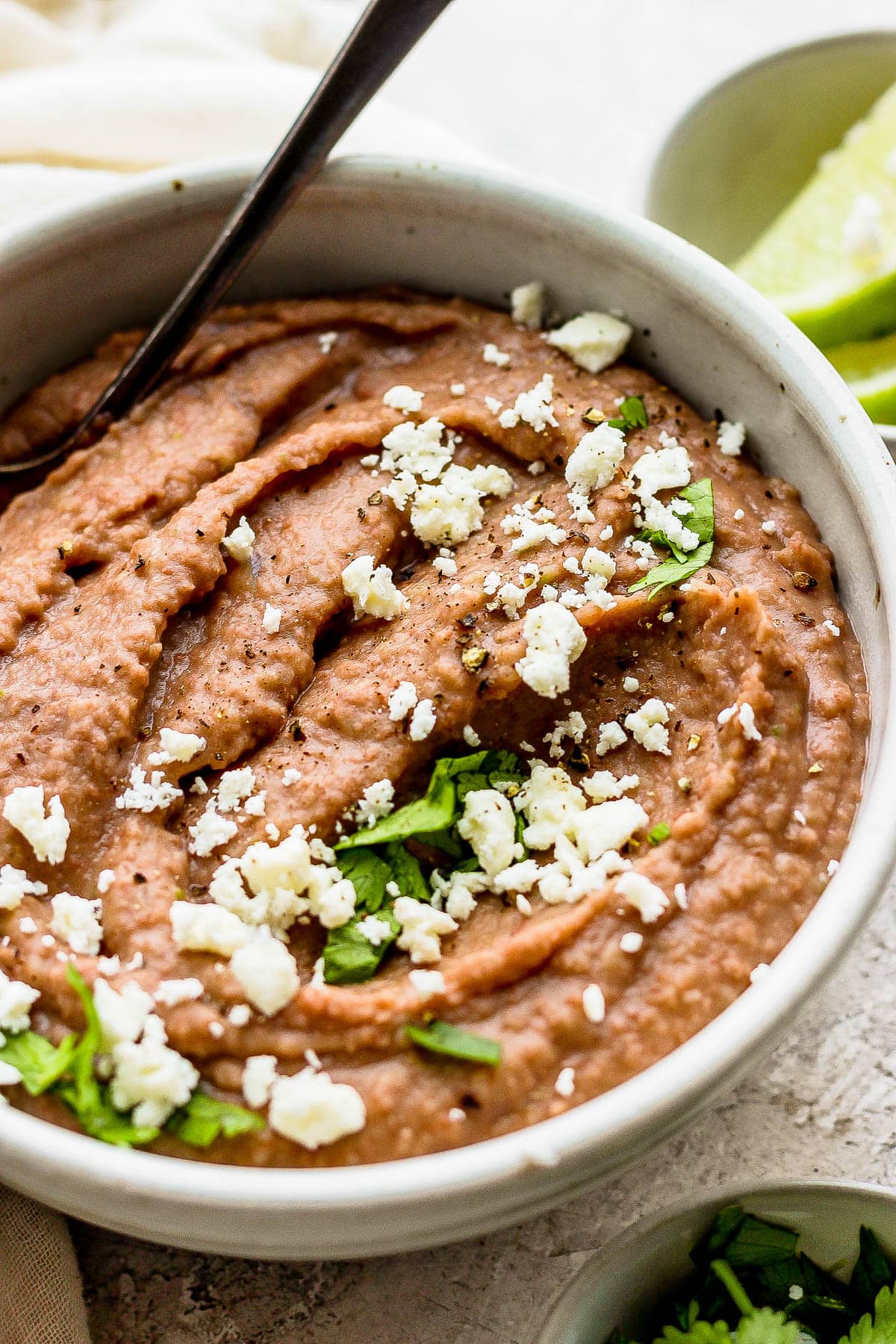 Refried beans in a bowl topped with cotija cheese, cilantro, and salt and pepper.