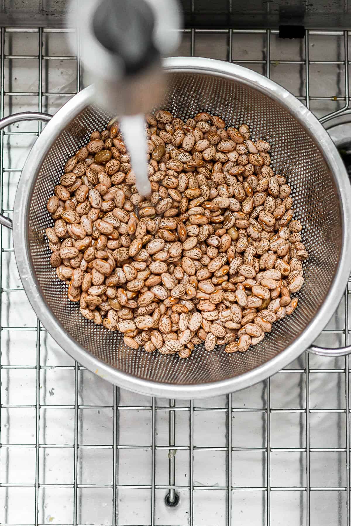 Dry pinto beans in a colander being washed and cleaned.