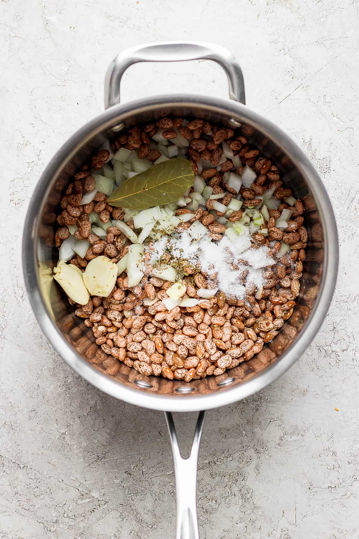 Dry pinto beans in a pot with onions, Mexican oregano, garlic, and a bay leaf.