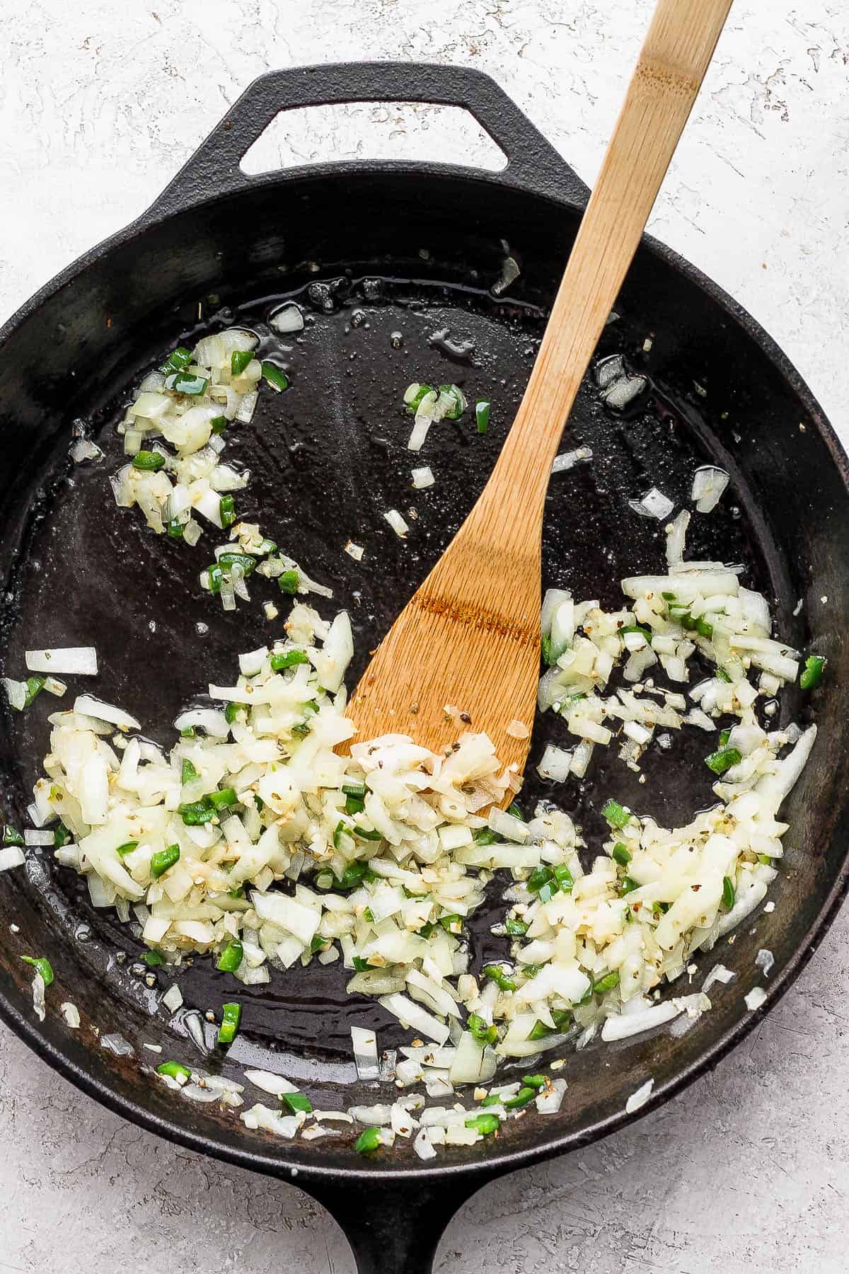 Onion, jalapeno, and garlic being sauteed in a skillet.