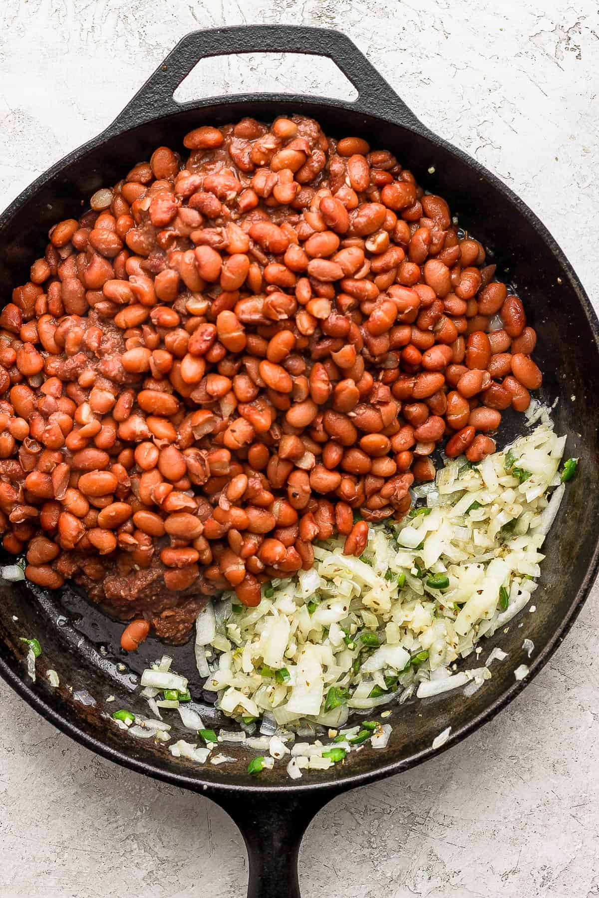 Cooked pinto beans in a skillet with onions, jalapenos, and garlic.