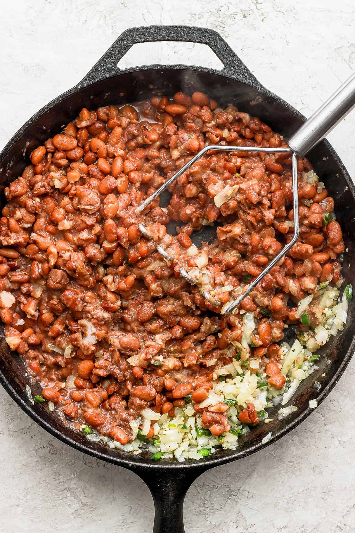 Pinto beans being mashed in a skillet to make refried beans.