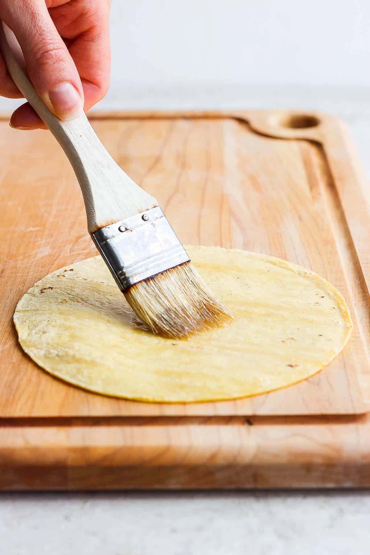 Brushing cooking oil on one side of a corn tortilla 