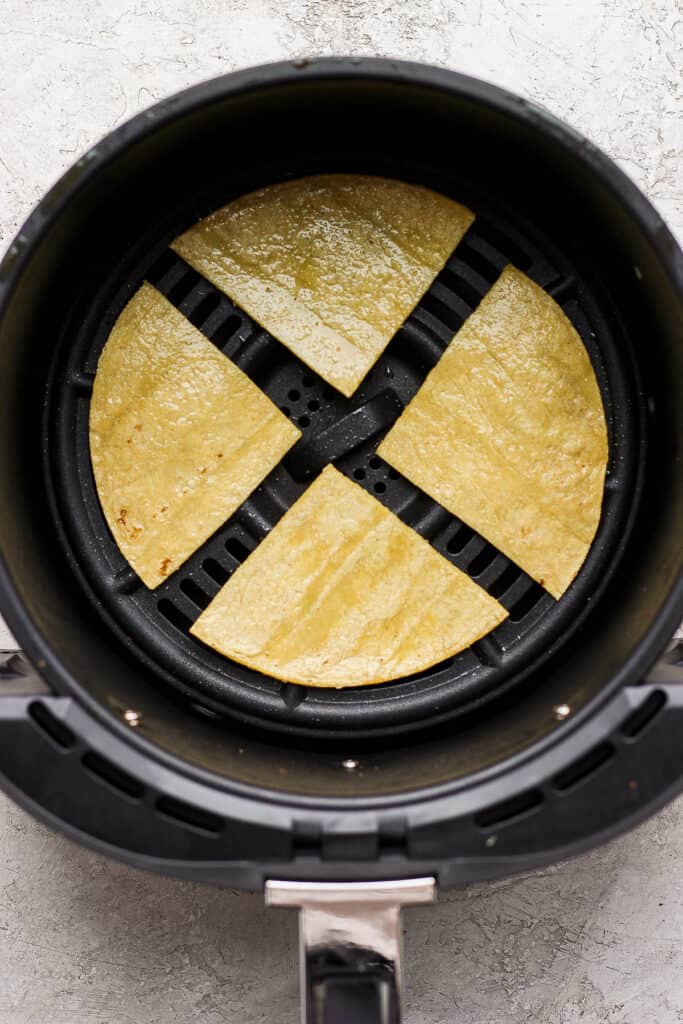Four tortilla pieces placed into the air fryer basket in a single layer