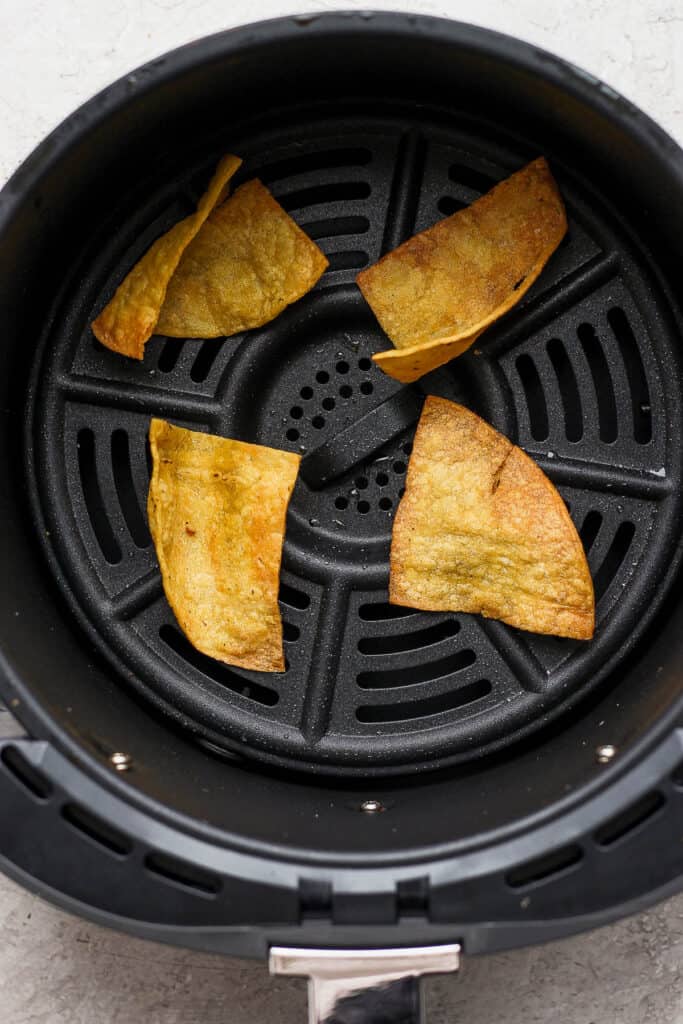 Four tortilla pieces in the air fryer basket after being fried in a single layer