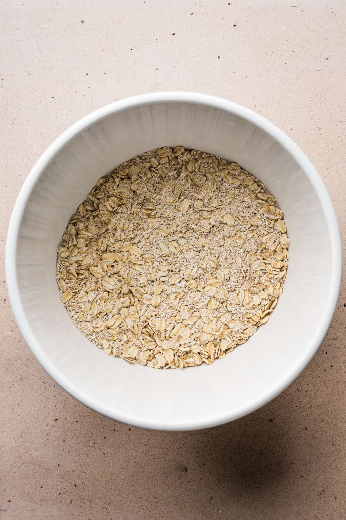 Ground oats, whole rolled oats, baking powder, ground cinnamon, and ground cloves in a mixing bowl.