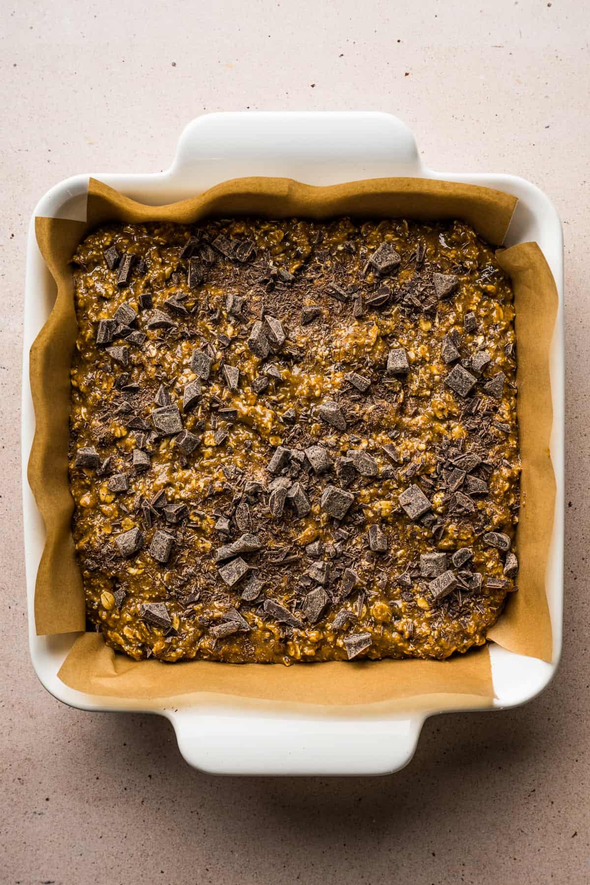 Chocolate Oat Bars batter in a baking dish lined with parchment paper.