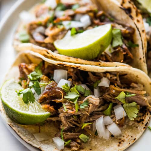 Carnitas (Mexican slow cooked pulled pork) in a corn tortilla topped with onion, cilantro, and lime.