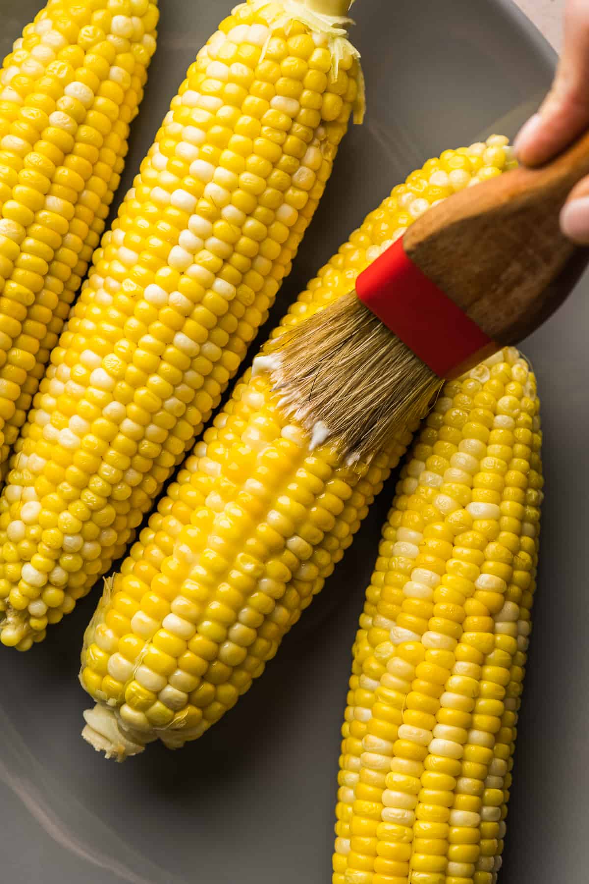 Ears of corn being brushed with melted butter.