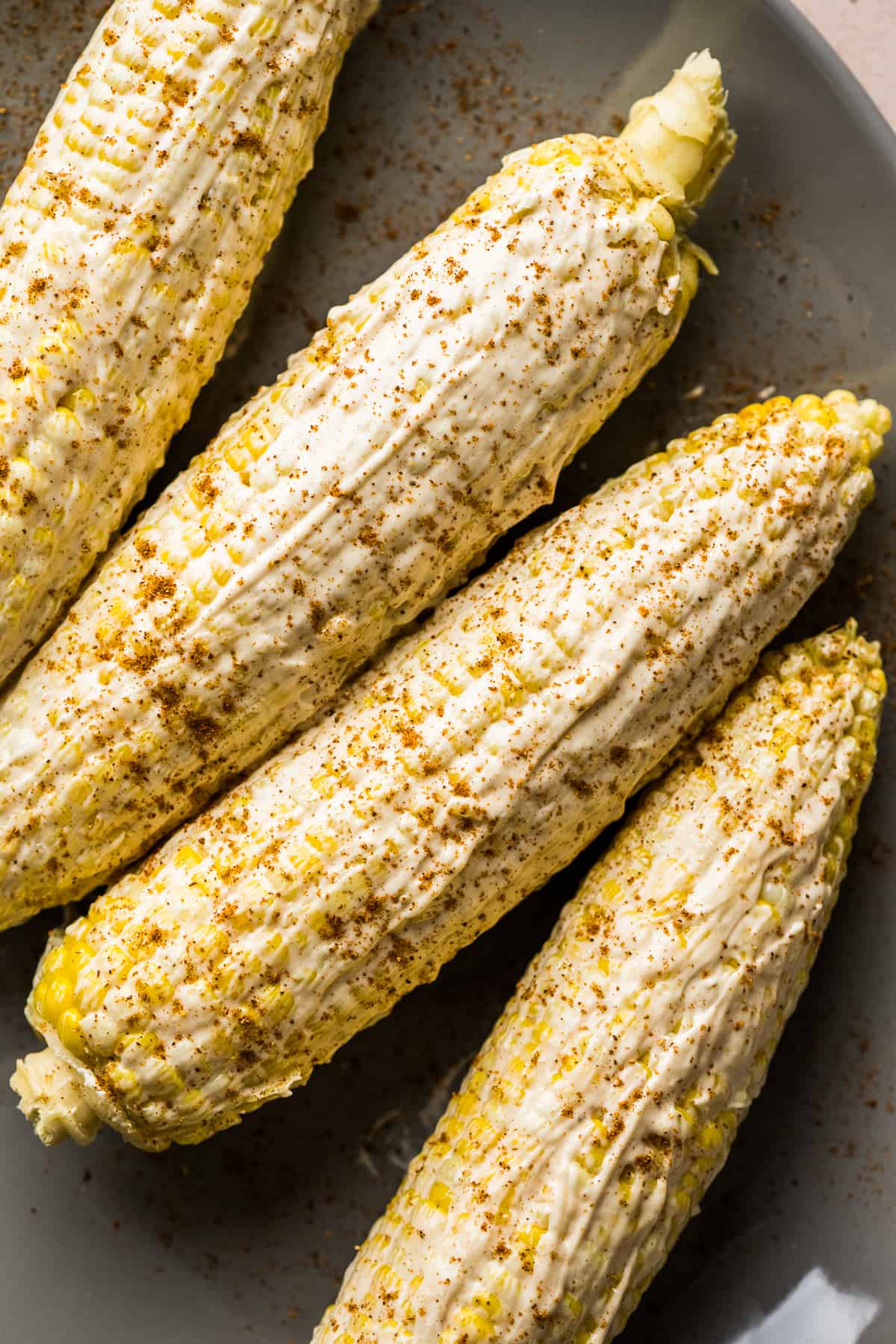 Elote on a serving platter slathered in a creamy mayo sauce and sprinkled with chili powder.