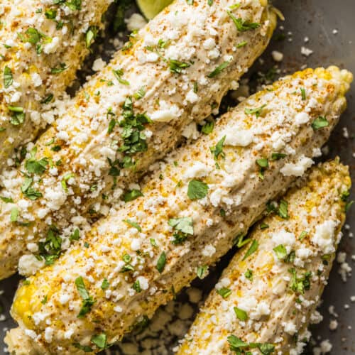 Elotes (Mexican Street Corn) on a plate with cotija cheese, cilantro, and mayo.