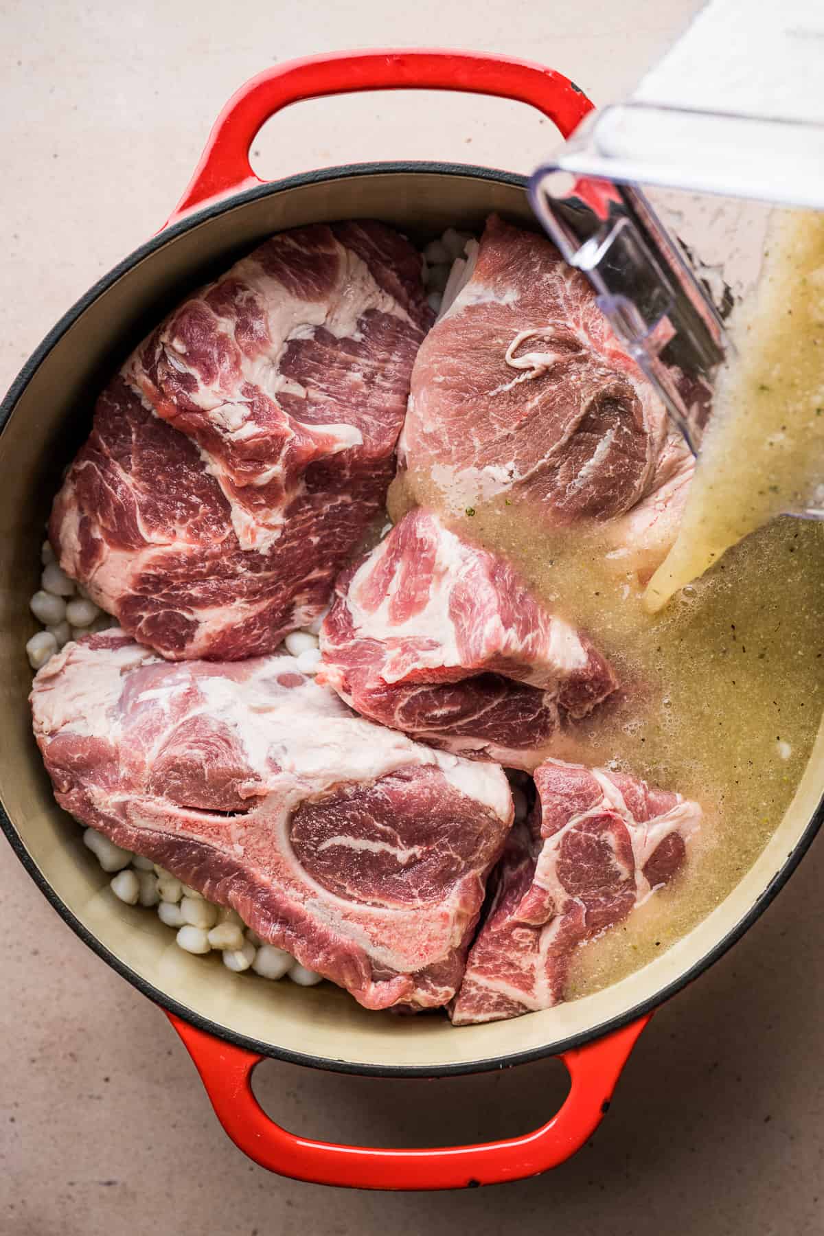 Blended broth being poured into a large pot with pork shoulder and hominy.