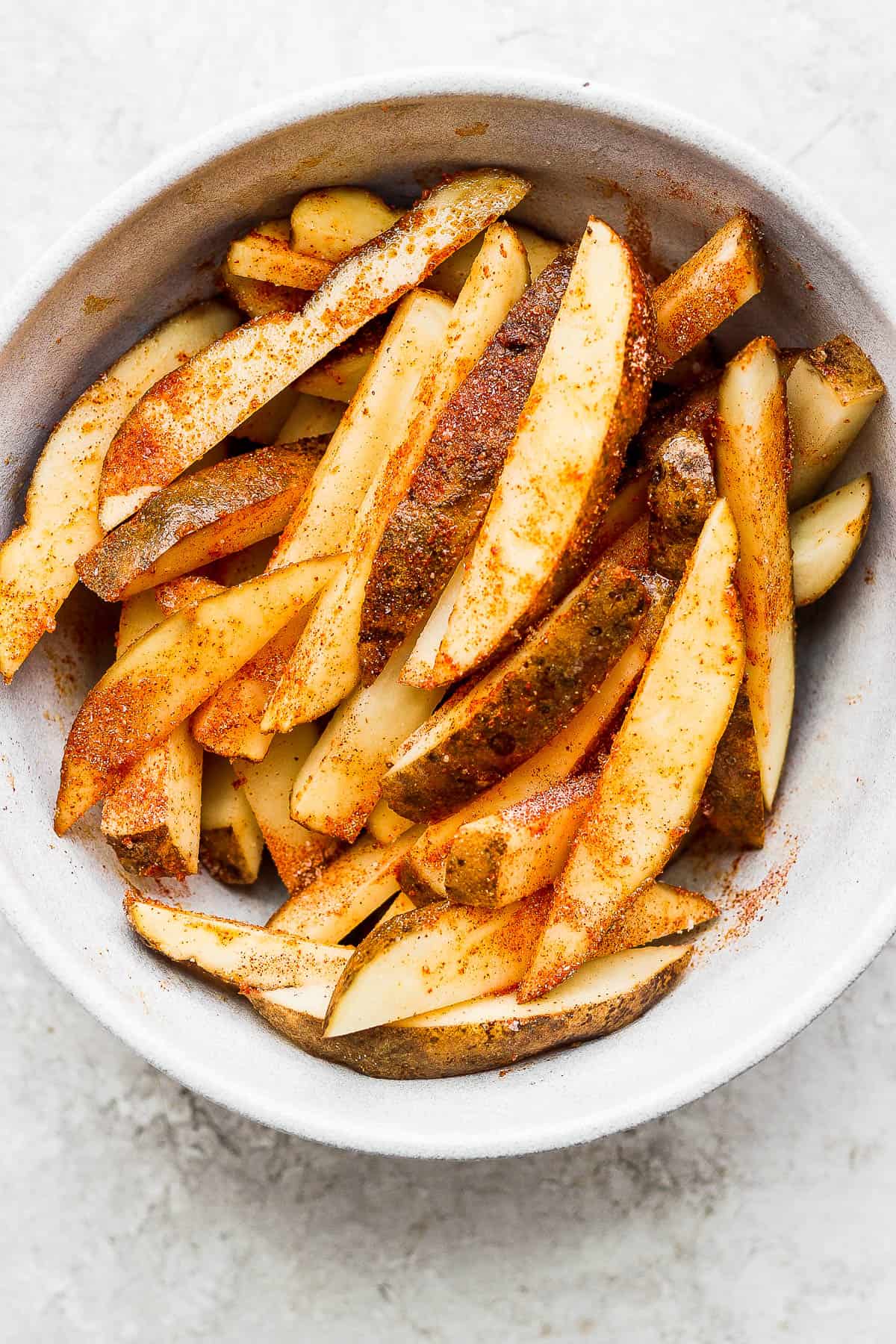 Cooked seasoned potato slices placed into a large bowl