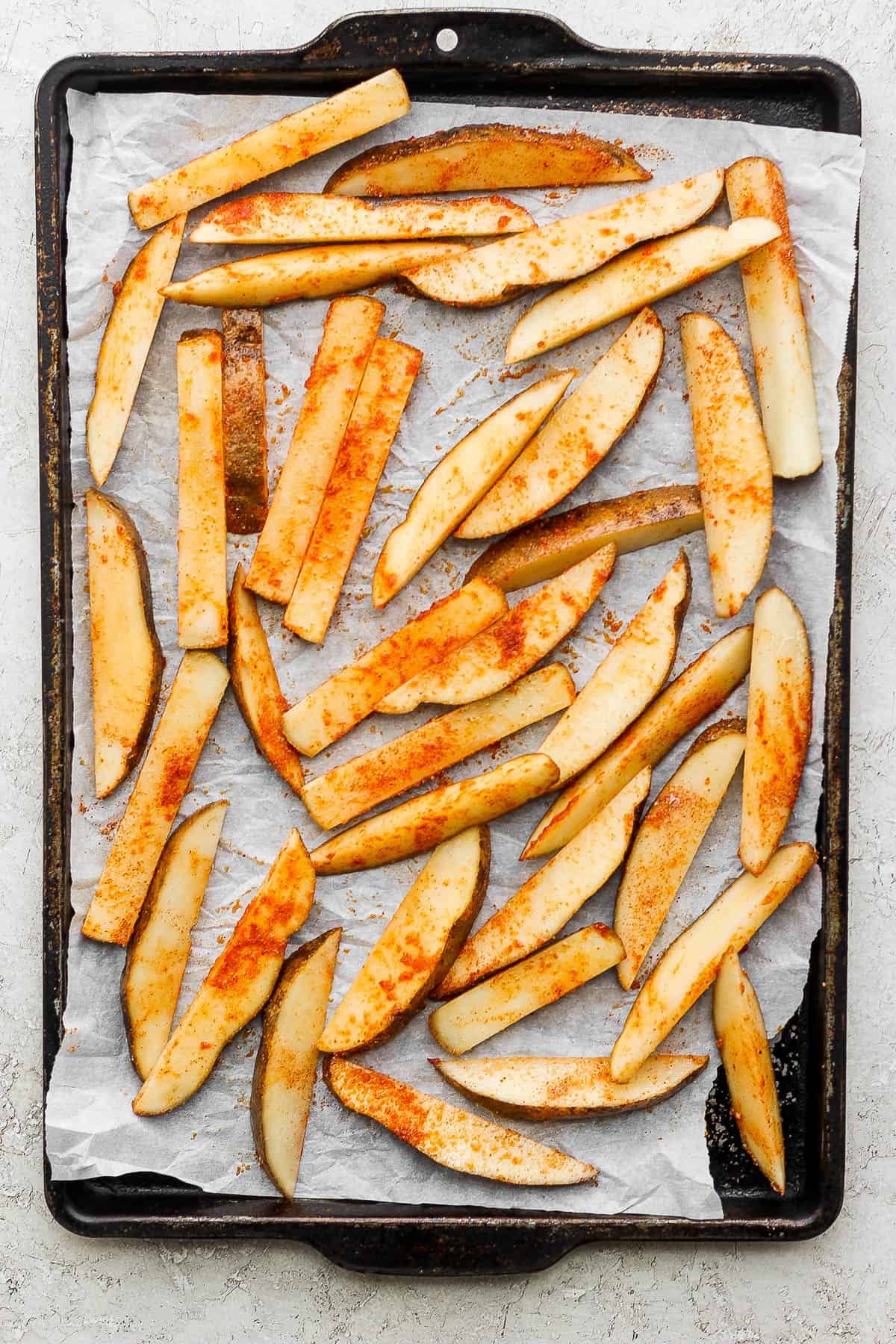 Potato fries sliced, seasoned, and placed on a large baking sheet lined with parchment paper. 