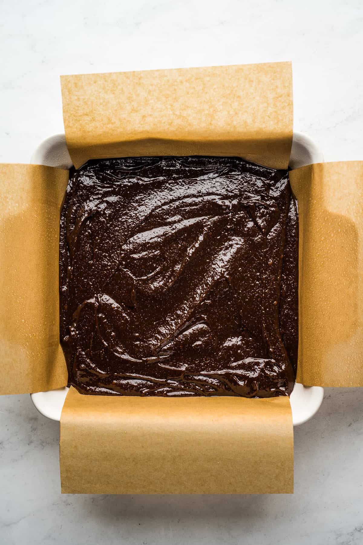Brownie batter in a square baking pan lined with parchment paper