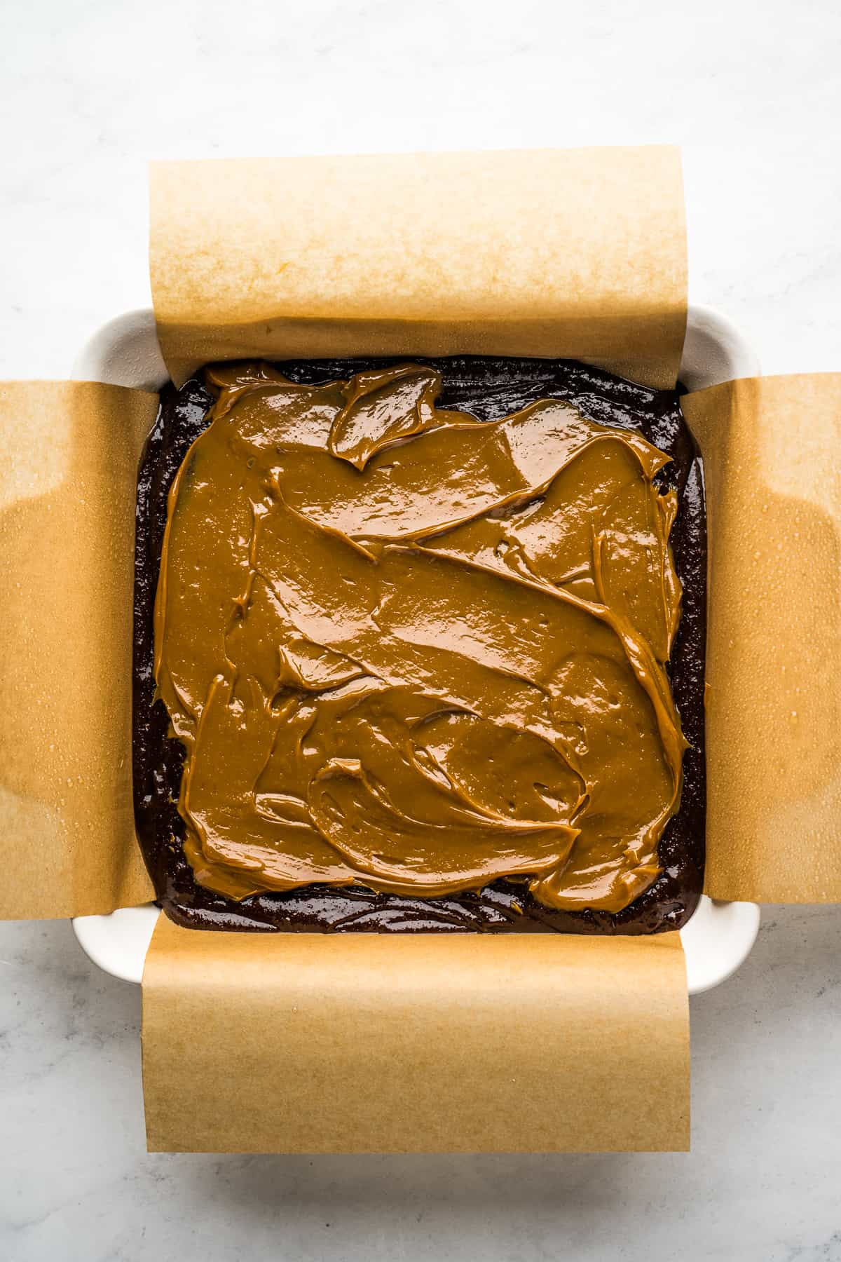 Brownie batter topped with a layer of dulce de leche on top in a square baking pan