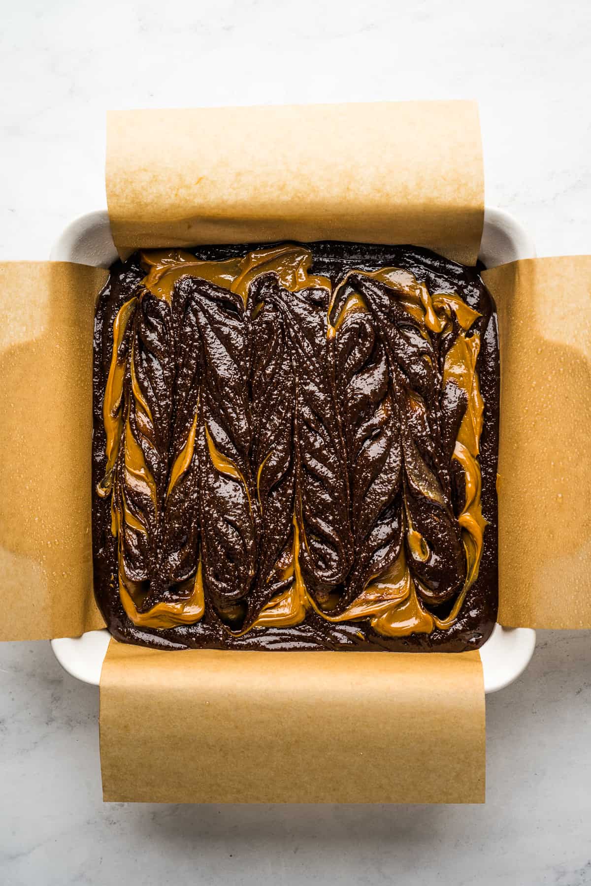 Dulce de leche brownie batter in a square baking dish lined with parchment paper