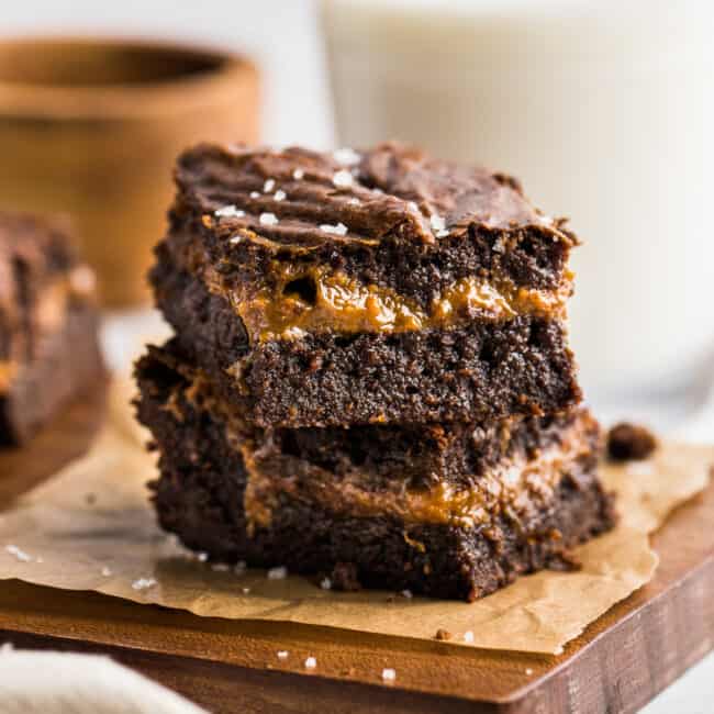 Dulce de Leche Brownies stacked on top of one another to showcase the layer of dulce de leche in the middle.