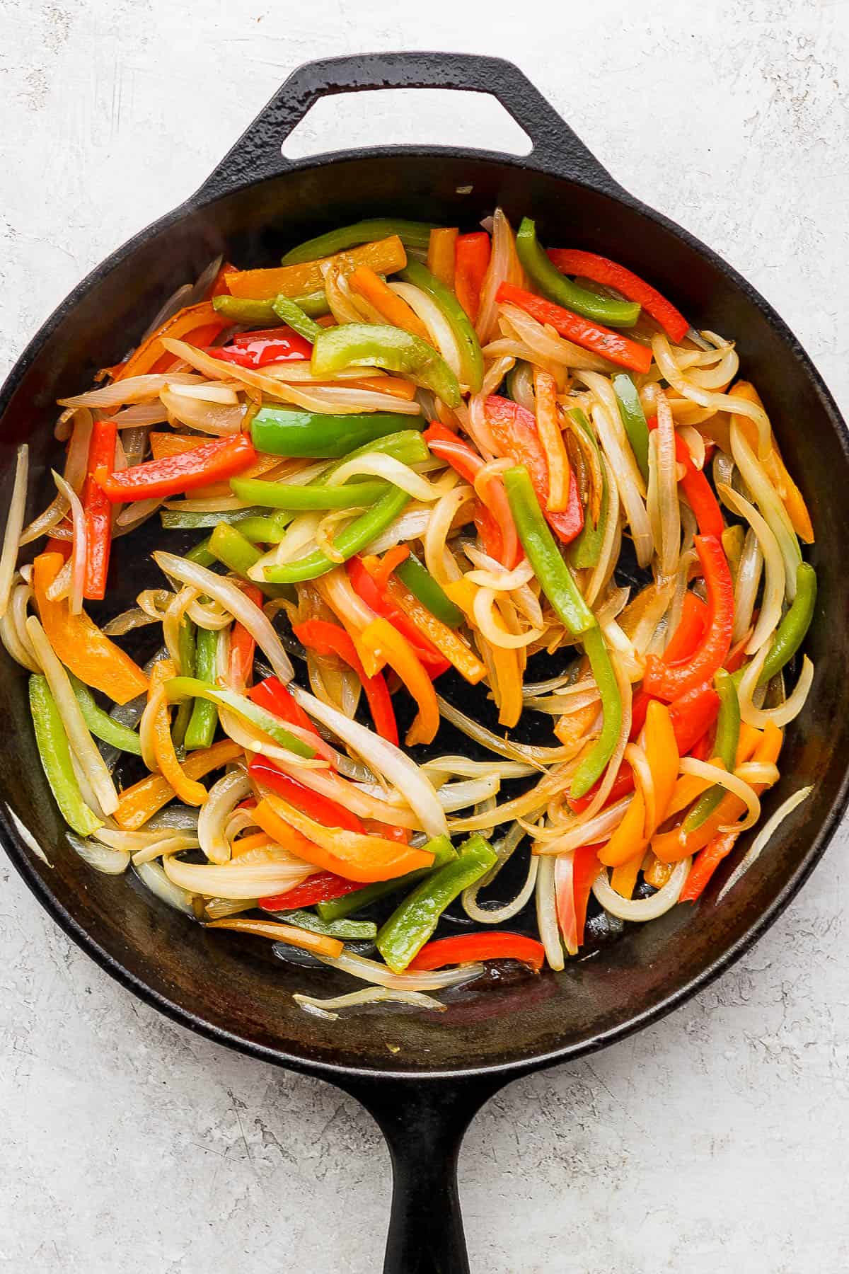 Softened and caramelized bell peppers and onions in a skillet.