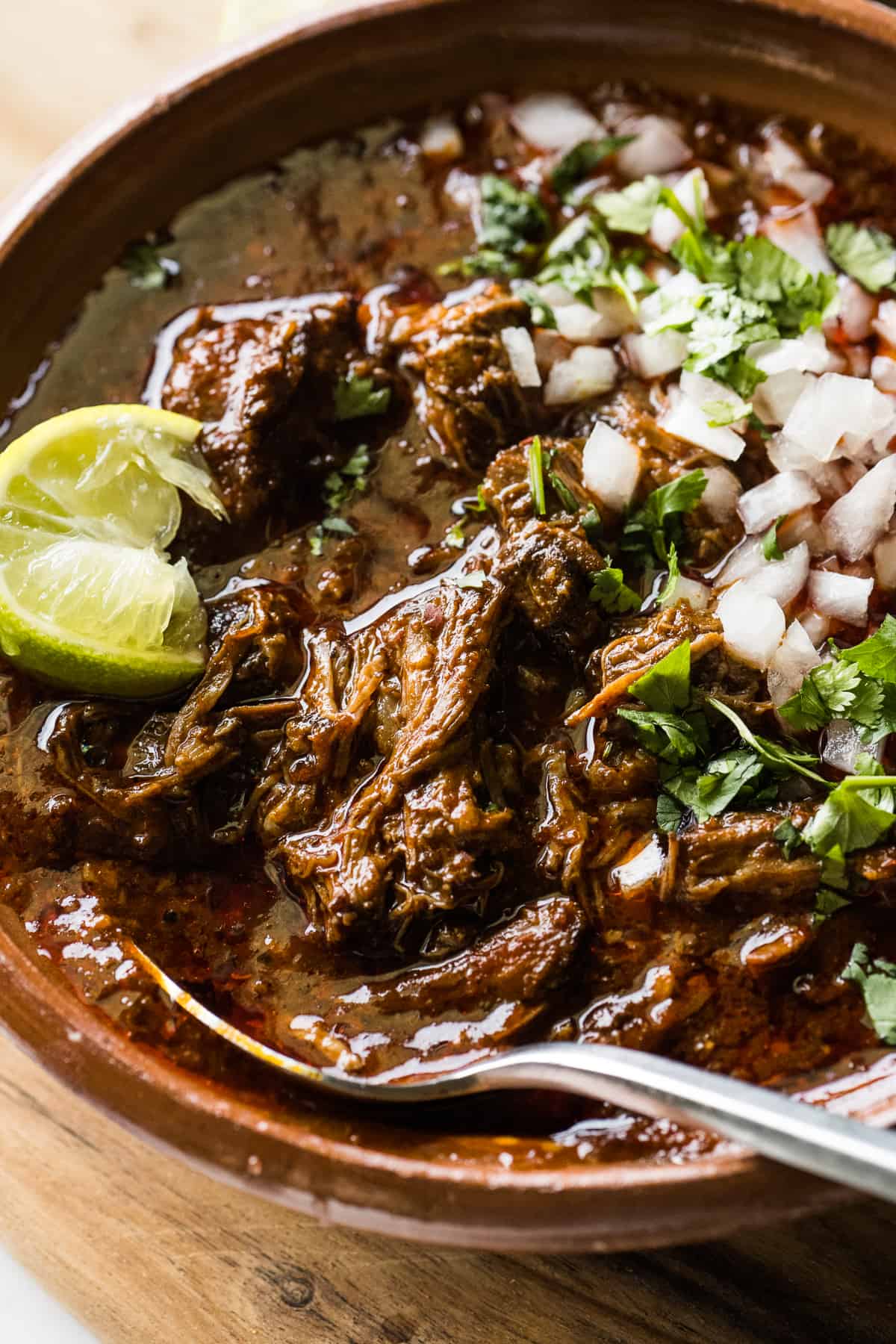 A bowl of birria topped with chopped white onions, cilantro, and a lime wedge.