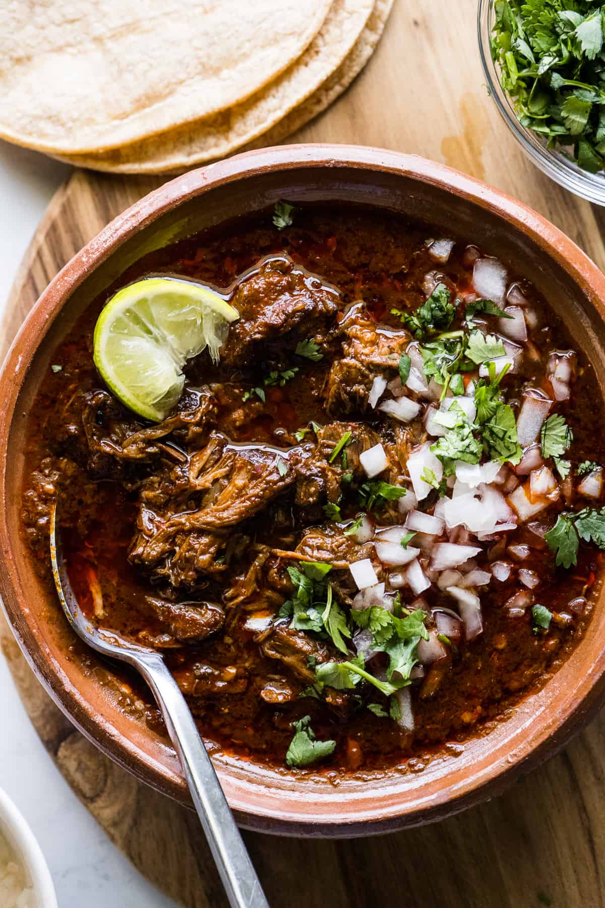 A bowl of beef birria topped with chopped cilantro, onions, and a lime wedge.