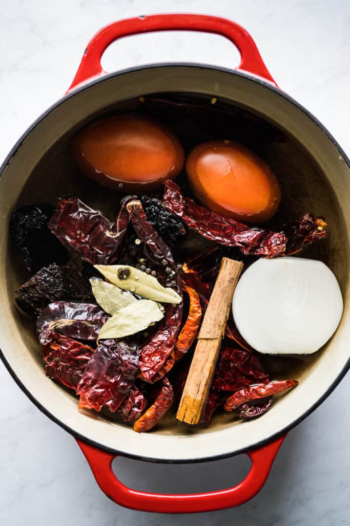 Dried chiles, tomatoes, onion, cinnamon, and spices in a pot for birria.