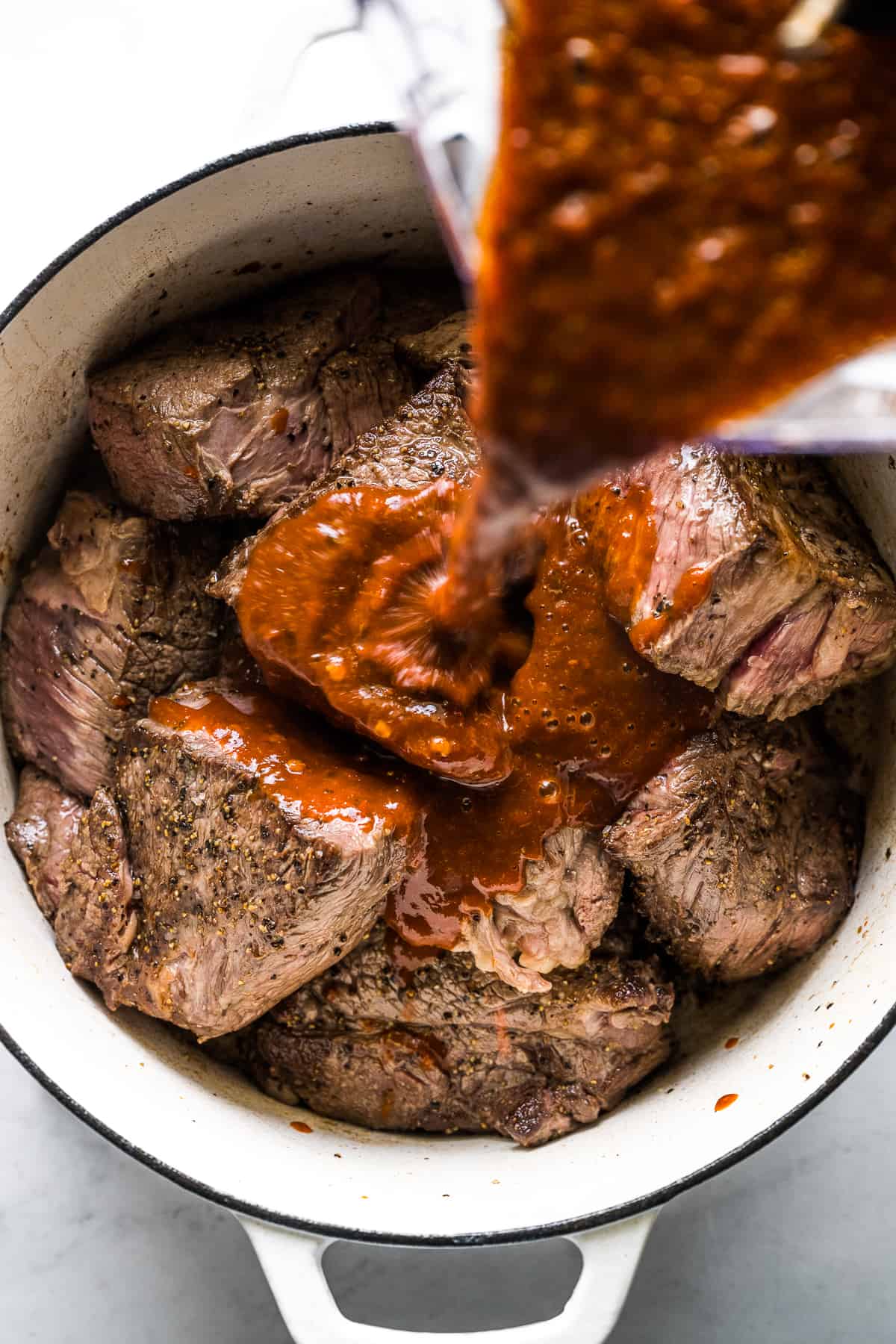 Red chile sauce being poured into a pot with chuck roast for birria.