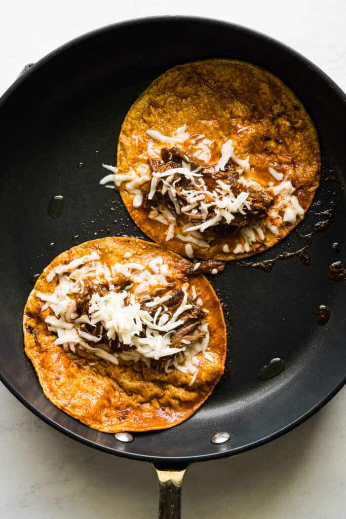 A birria taco being fried in a skillet filled with shredded birria and cheese.