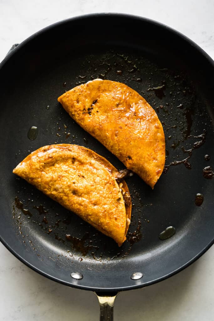 Birria tacos being fried in a skillet.