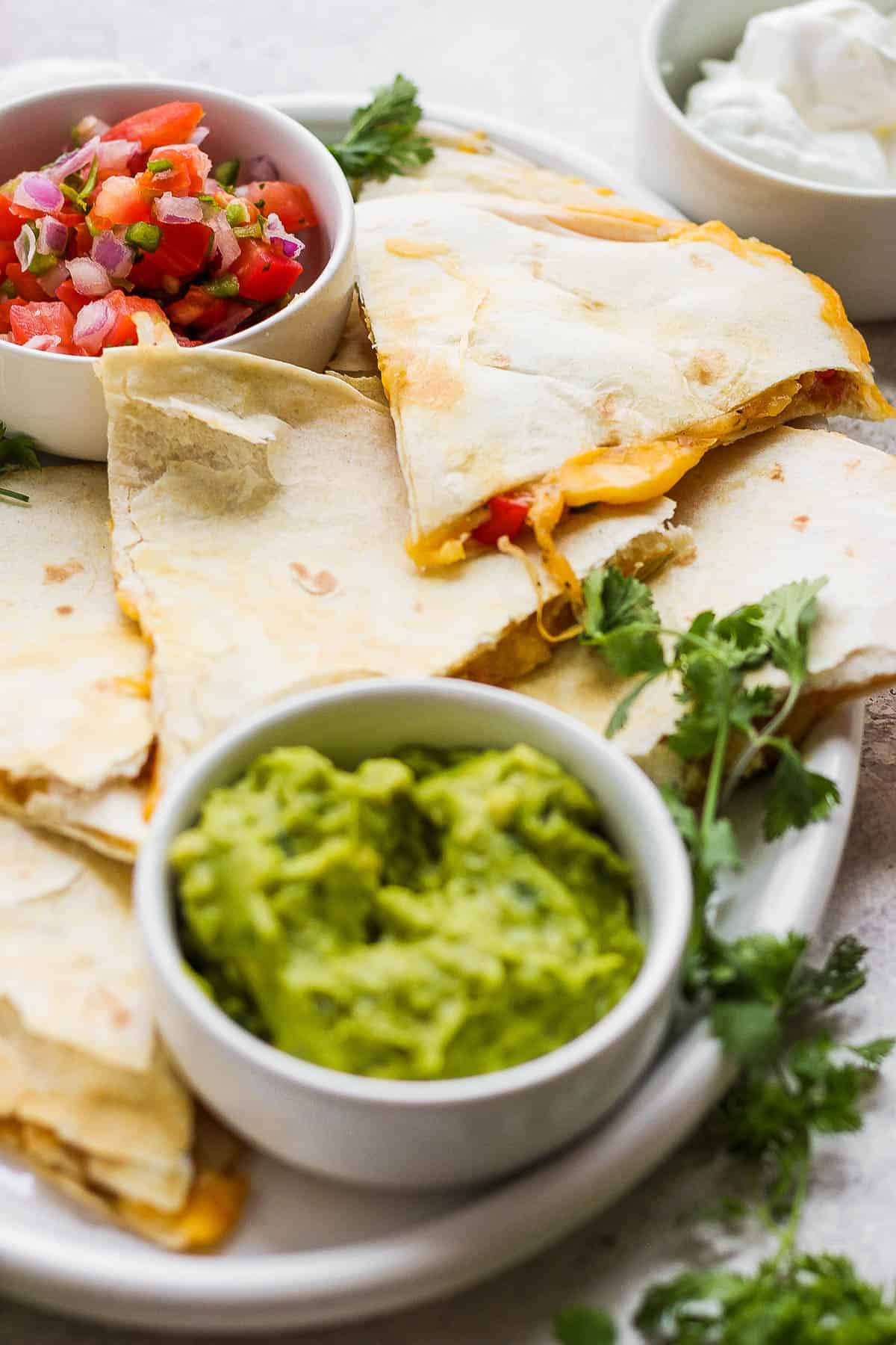 Cheesy chicken quesadillas on a plate served with pico de gallo and guacamole.