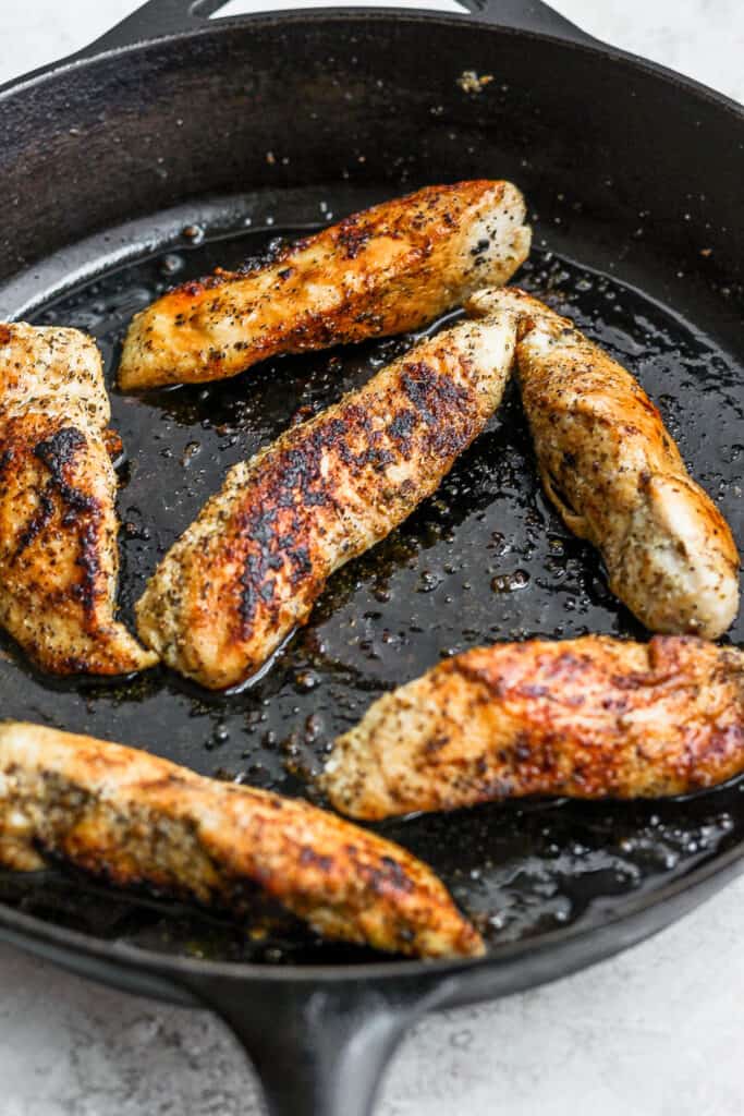 Chicken breasts cooking in a skillet for quesadillas.